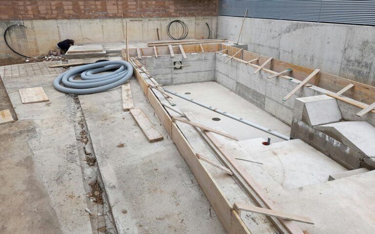 Construction site with wooden materials, pipes, and hoses on concrete